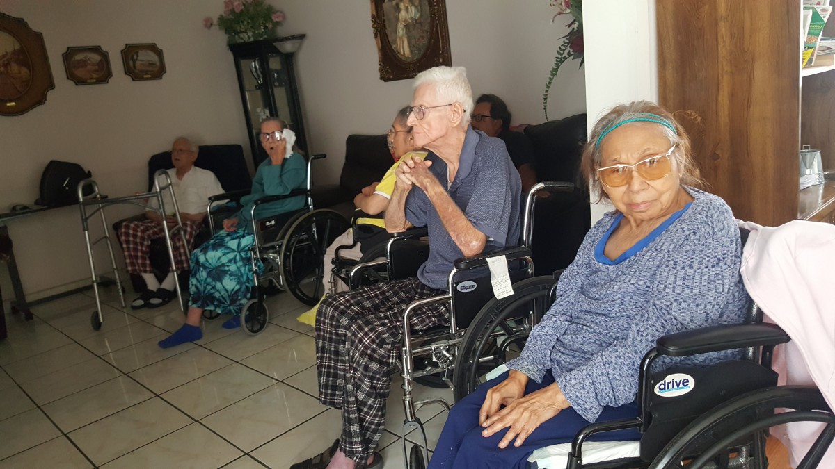 A group of elderly individuals sitting in wheelchairs indoors, engaged in a communal setting.