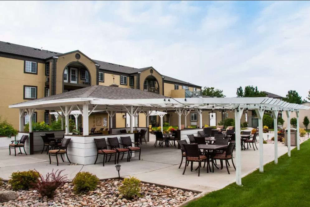A spacious outdoor patio with elegant seating arrangements under a pergola, situated in front of a modern building.