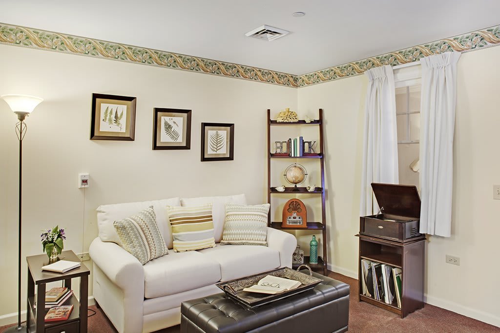 A cozy living room with a white sofa, decorative pillows, and a vintage-style bookshelf.