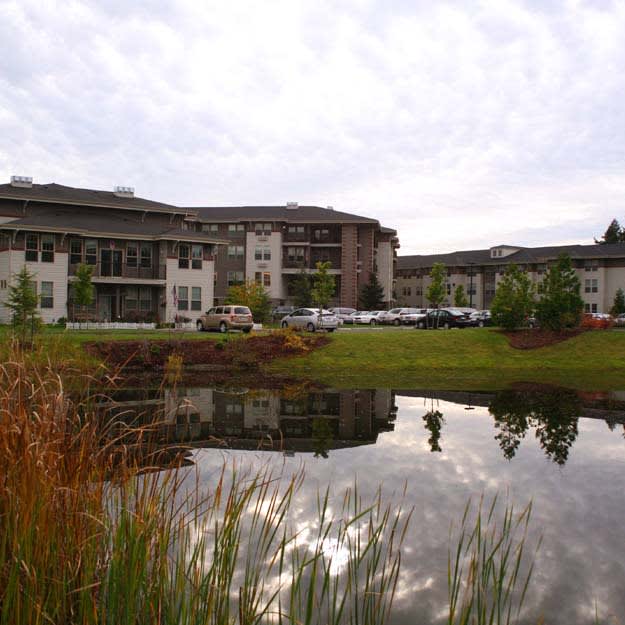 A modern building surrounded by nature, with a pond reflecting the sky and architecture.