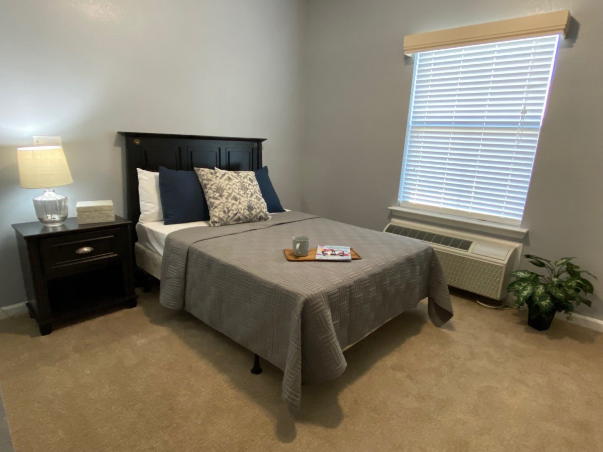A cozy bedroom with a neatly made bed, nightstand, and window.
