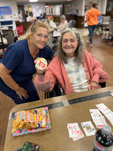 A caregiver shares a joyful moment with an elderly woman, celebrating with a decorated cookie during a fun activity.