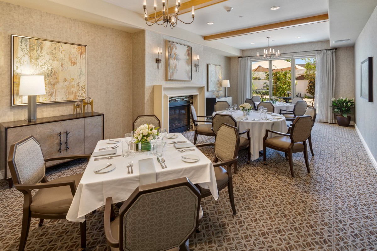 An elegant dining room with neatly arranged tables and upholstered chairs, featuring a chandelier and sophisticated decor.