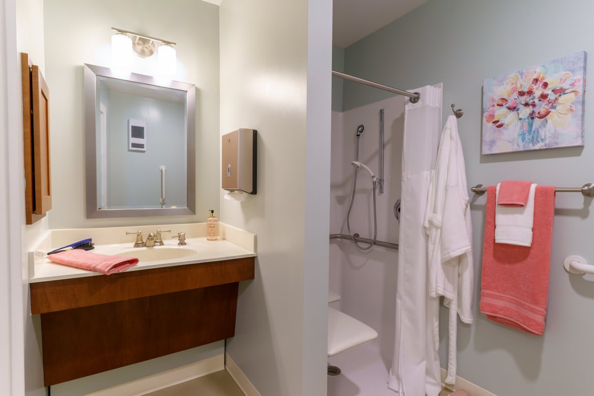 Modern bathroom with vanity, sink, and shower area equipped with robes and towels.