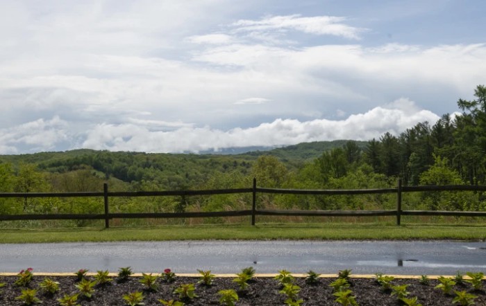 A scenic view of a lush green landscape with a wooden fence and cloudy sky.