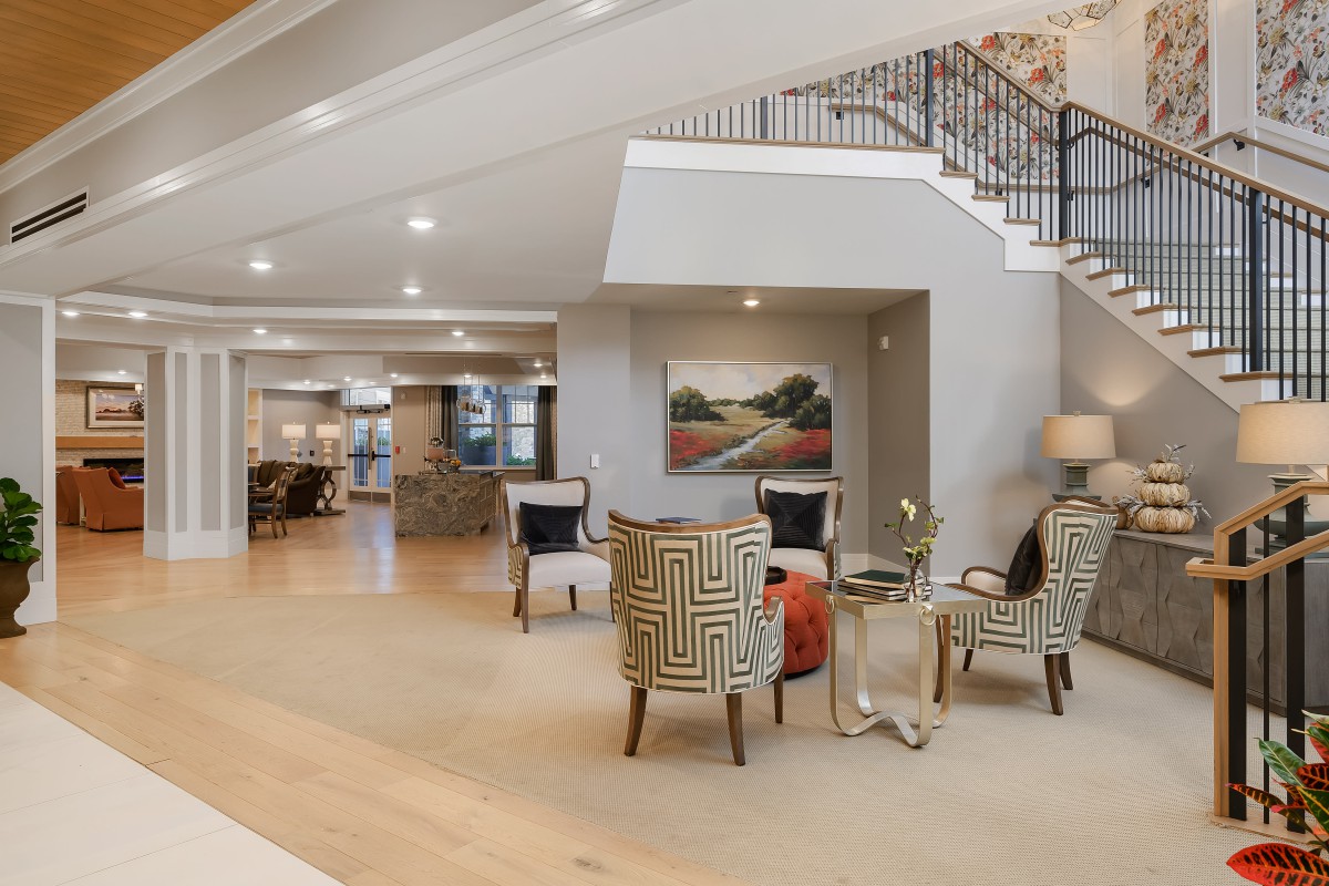 A modern living room with elegant seating, artwork, and a staircase.