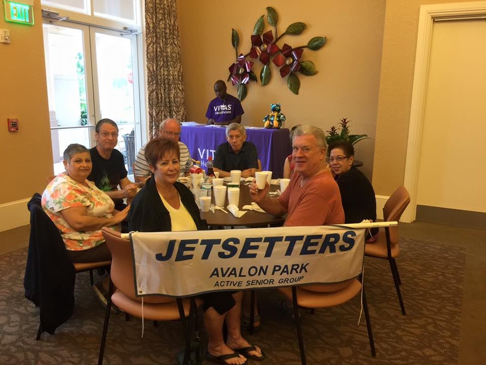 A group of people sitting together at a table with a 'Jetsetters Avalon Park' banner.