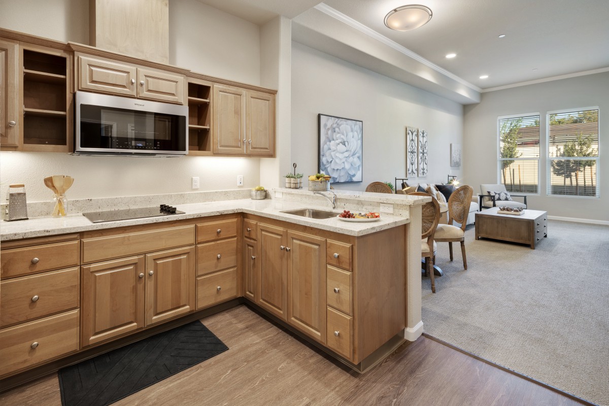 A modern kitchen with wooden cabinets and an open layout connected to a dining and living area.