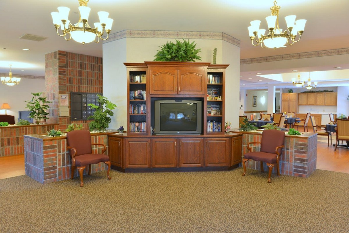 A cozy living room with a wooden TV stand, bookshelves, and comfortable chairs.