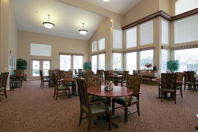 A spacious and well-lit dining area with multiple tables and chairs, featuring large windows.