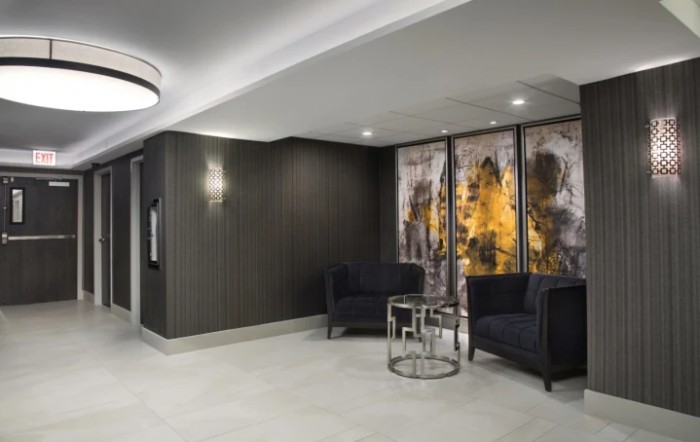 A modern lobby area featuring dark chairs, a decorative wall with artwork, and ambient lighting.