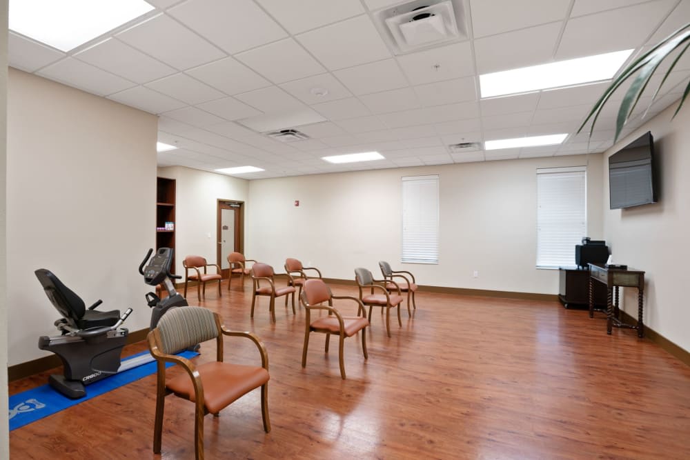 A well-lit exercise room with wooden flooring and several chairs arranged in a circular pattern.