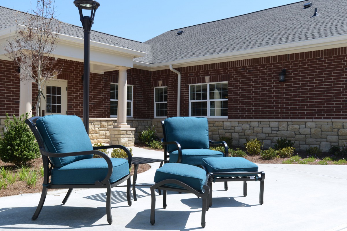 Outdoor patio with blue cushioned chairs and a brick building backdrop.