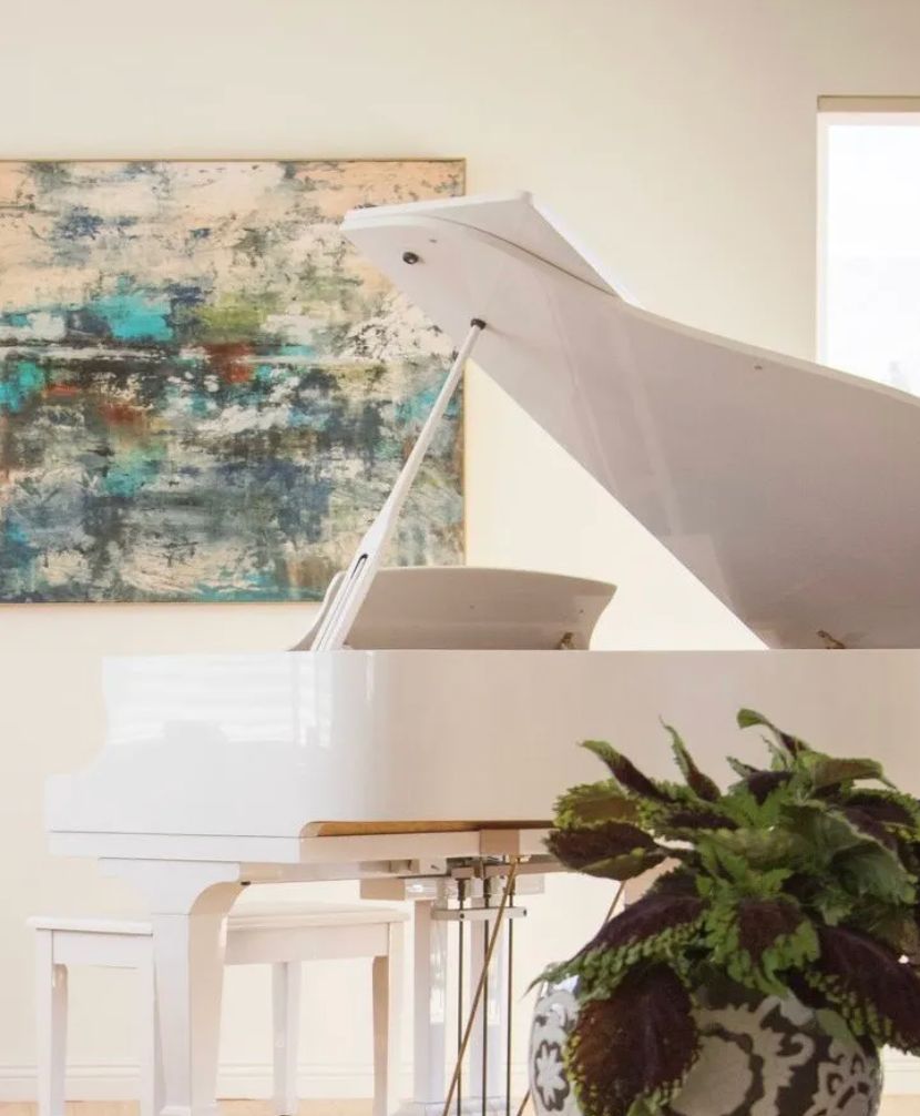A modern living room featuring a white grand piano and abstract artwork.