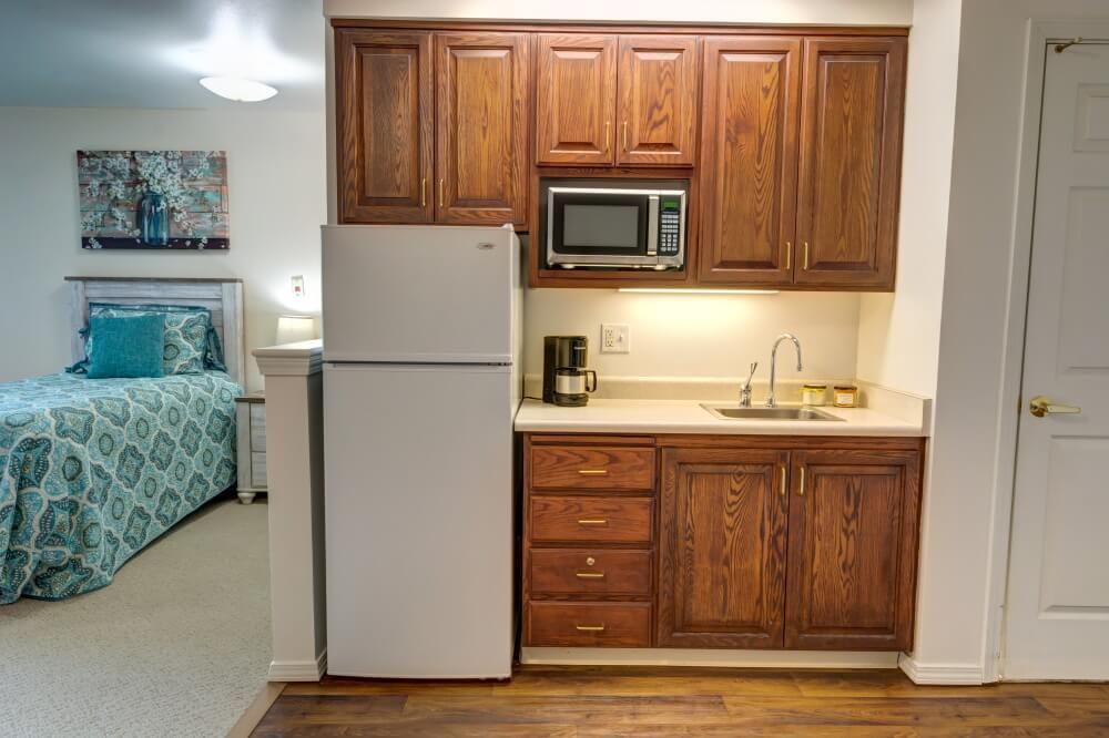 A compact kitchen area with wooden cabinets, a refrigerator, microwave, sink, and coffee maker.