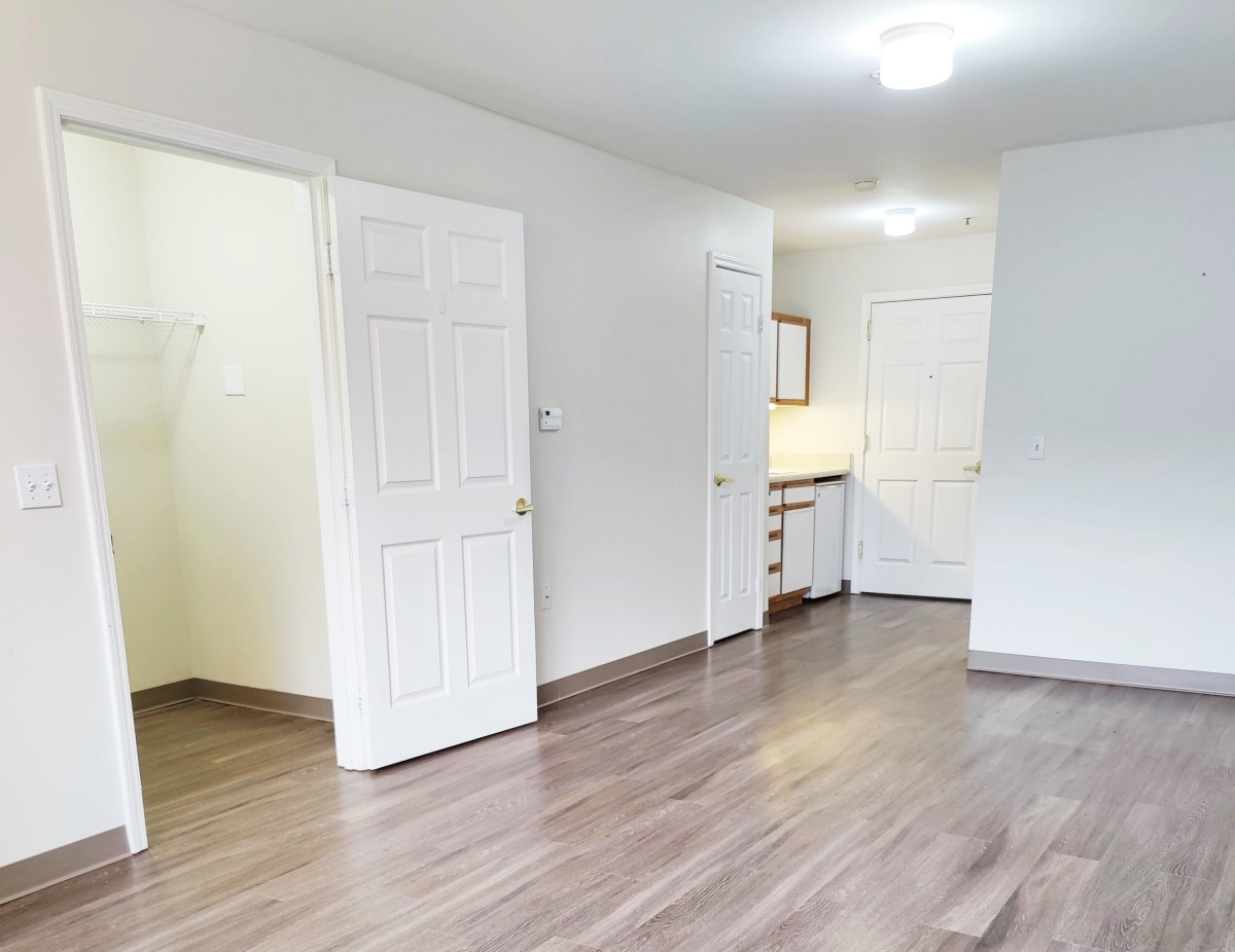An empty room with wood flooring, open doors, and bright lighting.