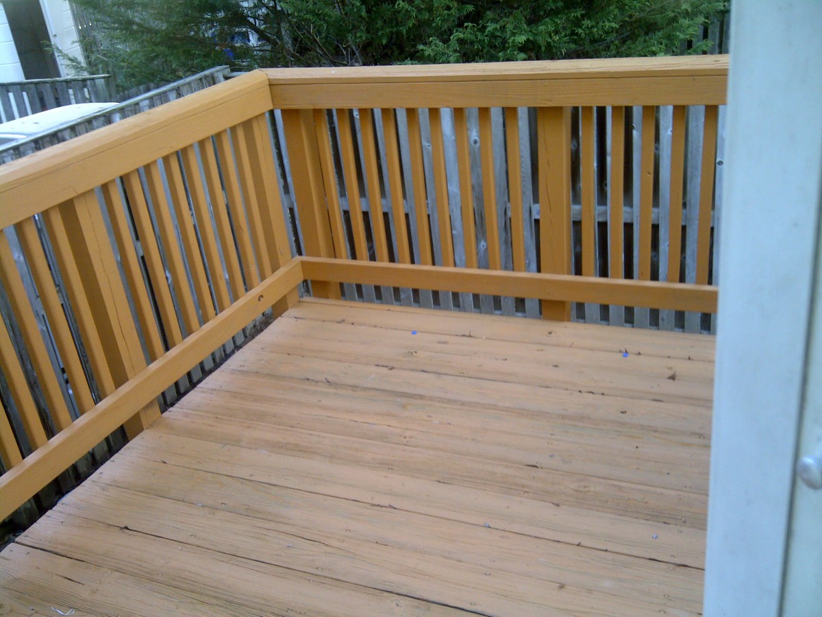 A small, empty wooden deck with a railing, overlooking greenery.