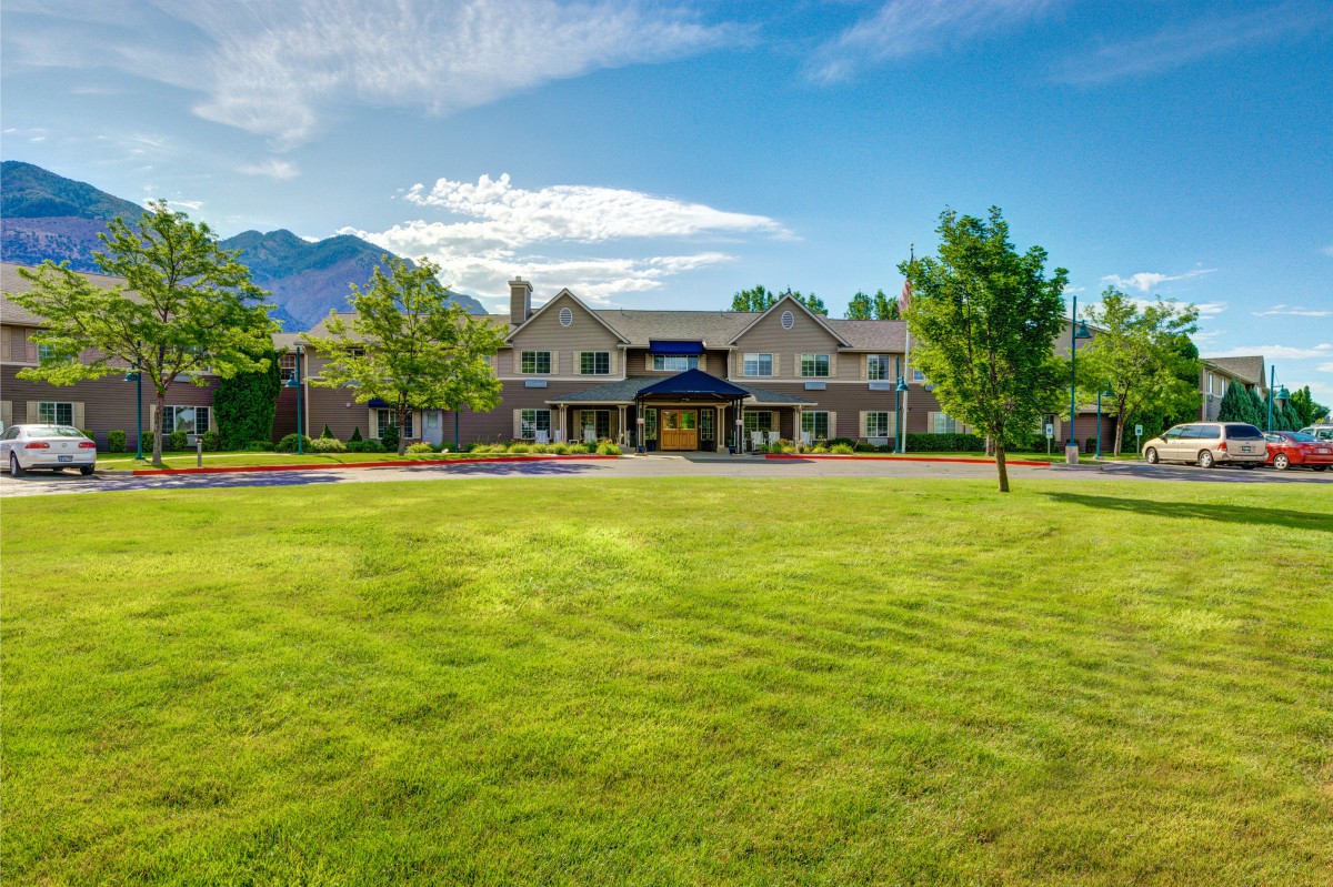 A large building with a sprawling lawn and mountain backdrop under a clear blue sky.