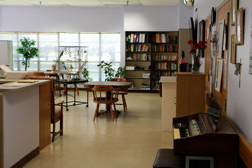 A serene library space featuring wooden tables, a wall of bookshelves, and indoor plants.