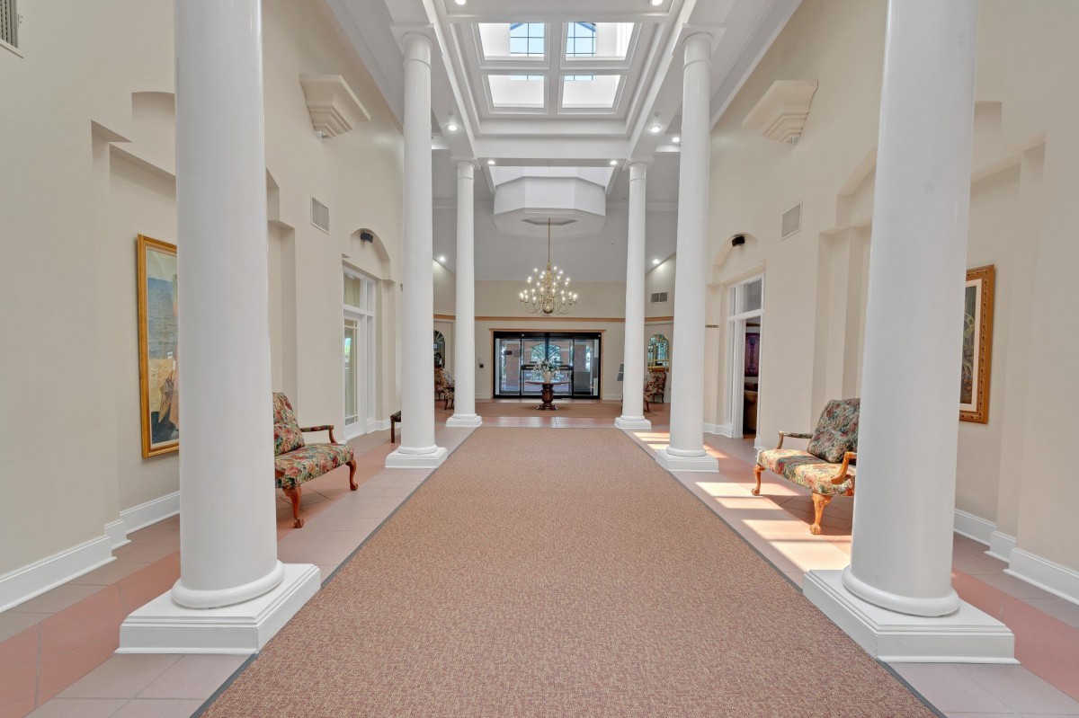 A spacious hallway with tall columns and a skylight, featuring elegant furniture and a chandelier.