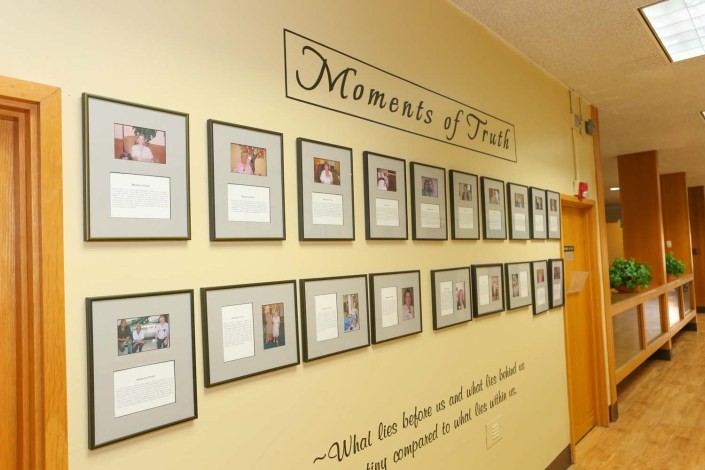 A hallway wall displaying a series of framed photographs titled 'Moments of Truth' with accompanying quotes.