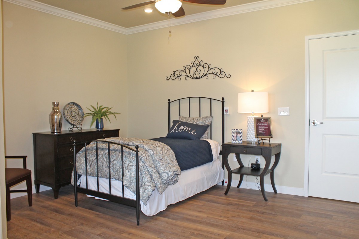 A cozy bedroom with a single metal frame bed, a nightstand with a lamp, and decorative wall art.