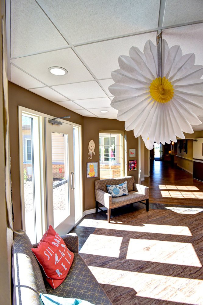 A brightly lit lobby area with decorative elements, including a large daisy hanging from the ceiling and comfortable seating near the entrance.