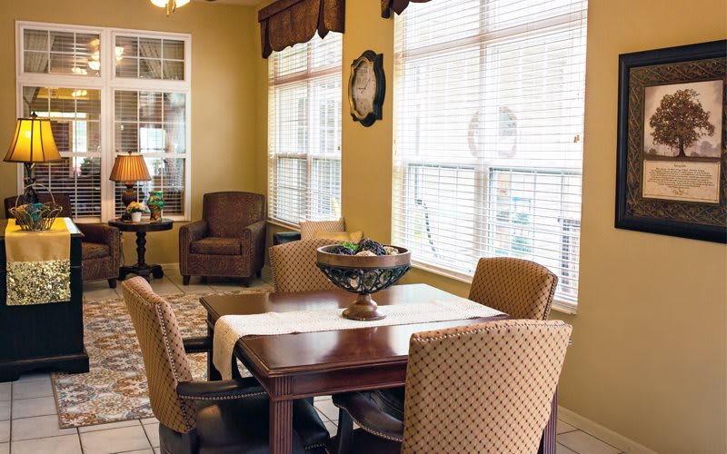 A cozy dining area with a wooden table, surrounded by chairs and illuminated by natural light from the large windows.