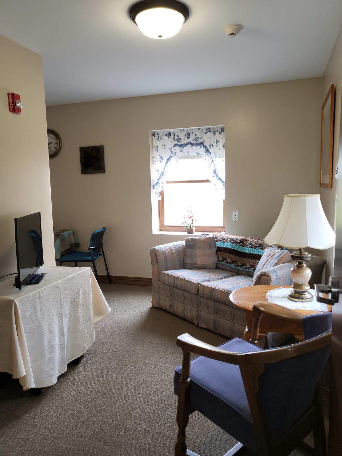 A cozy living room with a sofa, lamp, and television near a window.