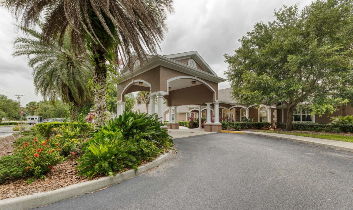 A building entrance with a driveway lined by palm trees and landscaped greenery.