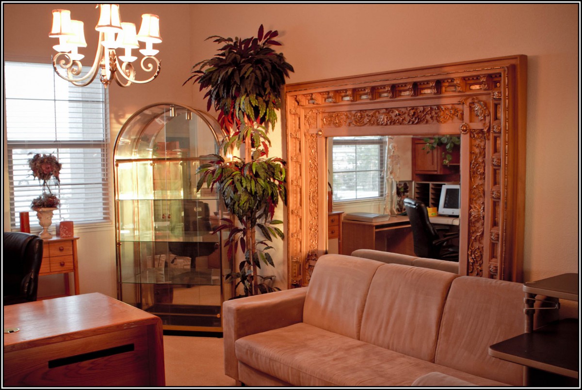 A cozy living room with a sofa, large mirror, indoor plant, and elegant chandelier.