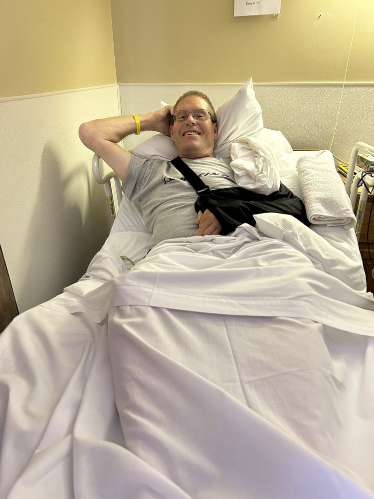 A patient resting in a hospital bed with an arm in a sling.
