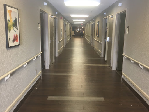 A well-lit hallway showcasing rooms with doors on either side, featuring a wooden floor and artwork on the walls.