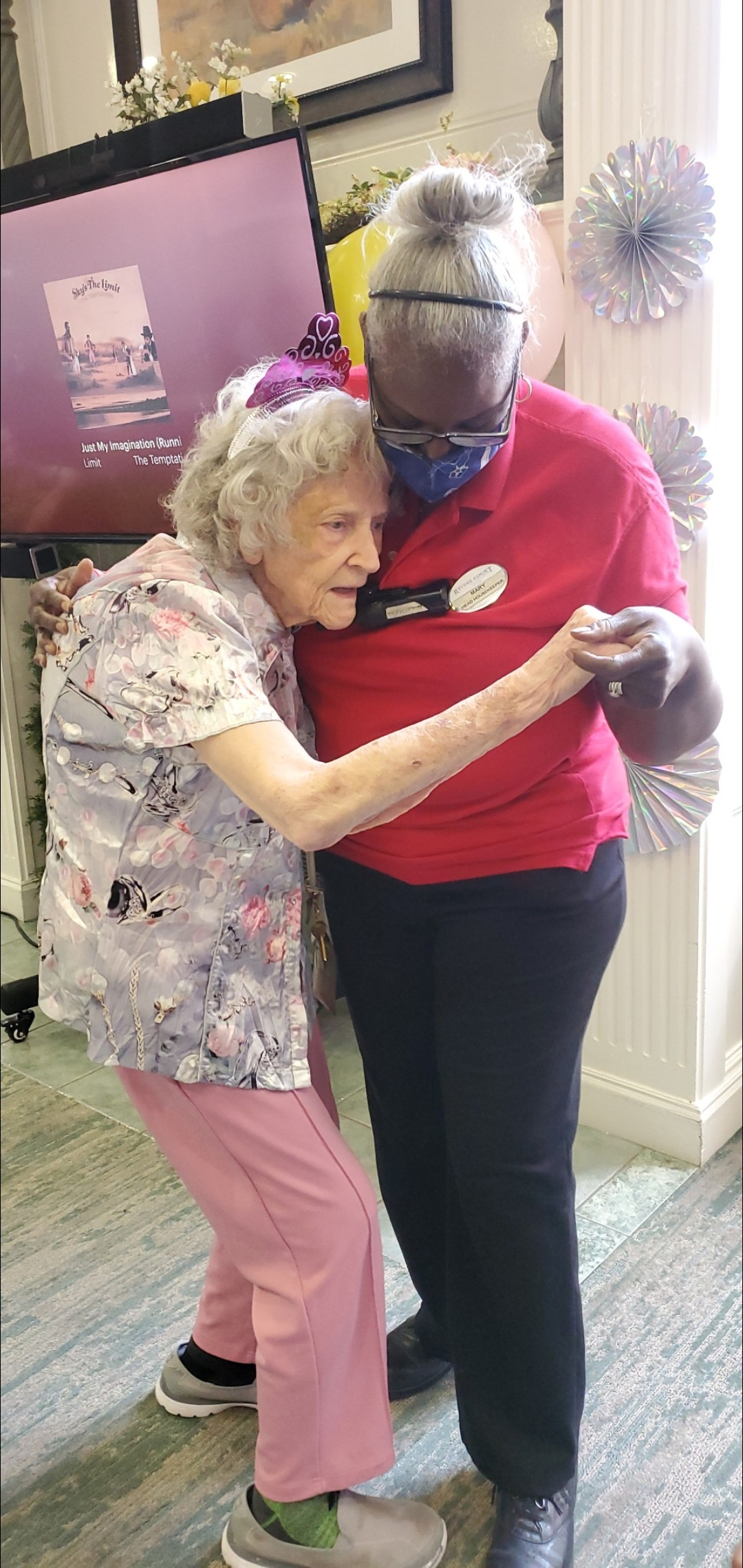 An elderly woman and a caregiver share a comforting embrace in a supportive environment.