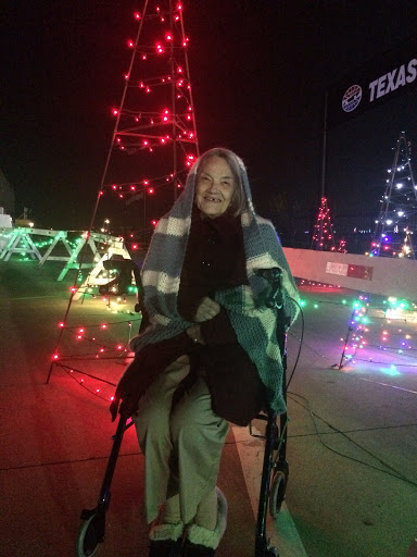 A person wrapped in a blanket sits amidst vibrant Christmas lights, enjoying the festive atmosphere.