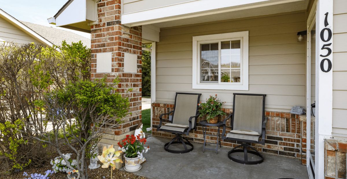 A cozy front porch with two chairs, a brick pillar, and decorative plants.