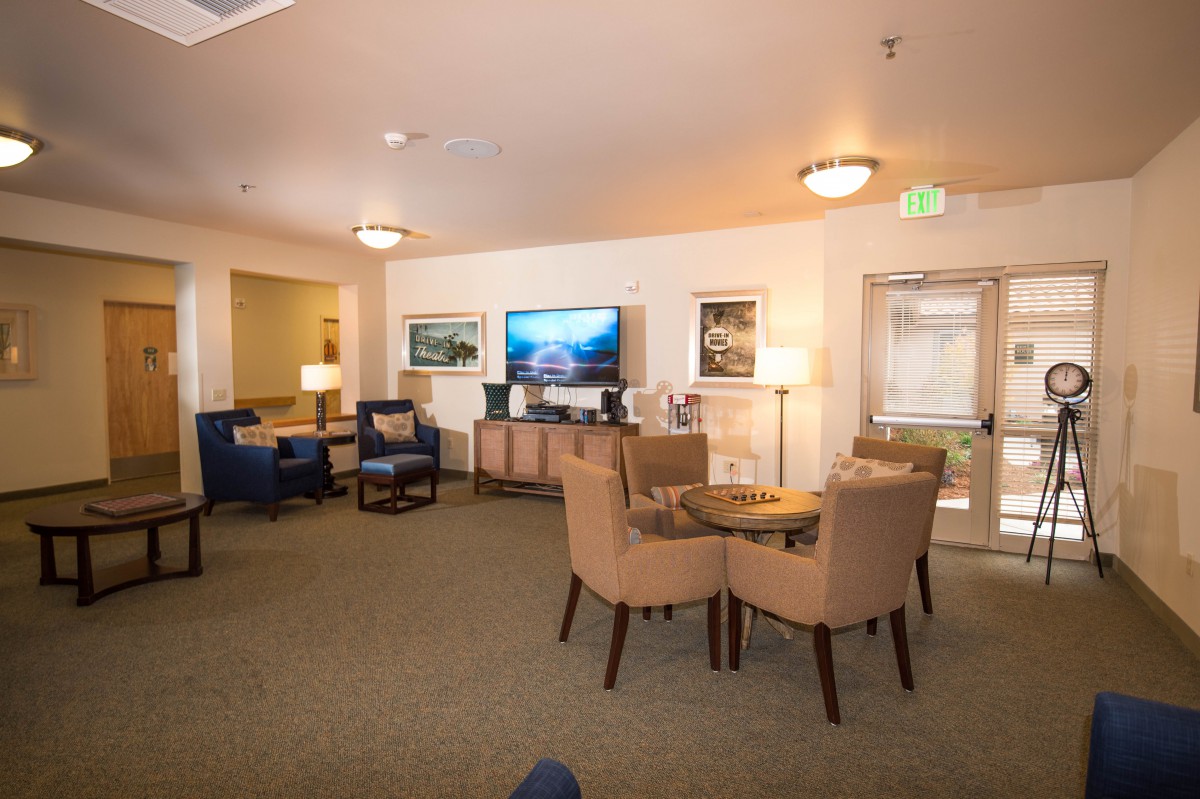 A cozy living room with comfortable seating and a large television, illuminated by warm lighting.