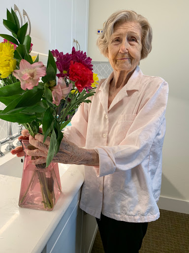 An elderly woman proudly holds a beautiful bouquet of colorful flowers in her home.