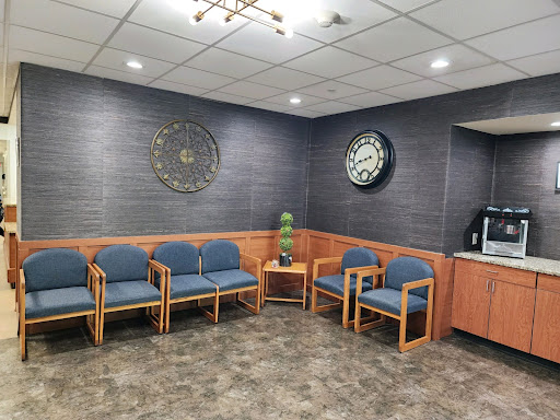 A cozy waiting area featuring wooden chairs and two decorative clocks.