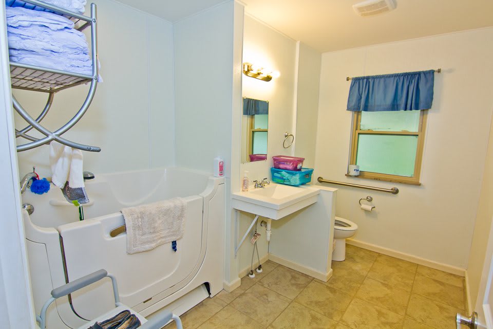 An accessible bathroom featuring a walk-in bathtub, sink, and toilet with grab bars for support.