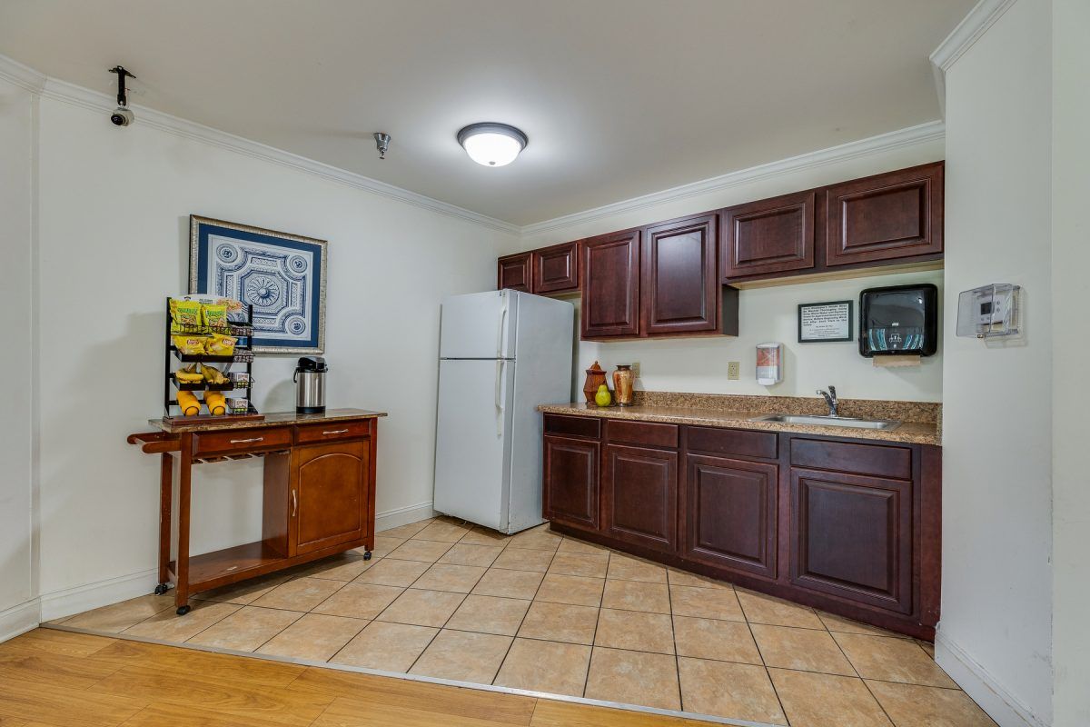 A kitchen with dark wooden cabinets, a refrigerator, and a tiled floor.