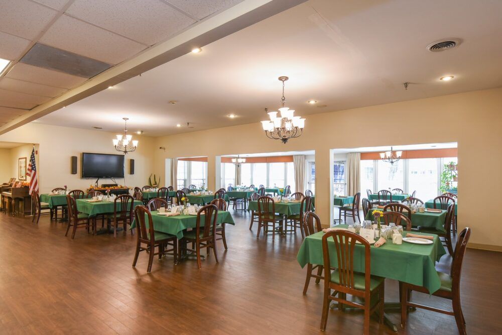 A spacious dining room with tables set and chandeliers hanging from the ceiling.