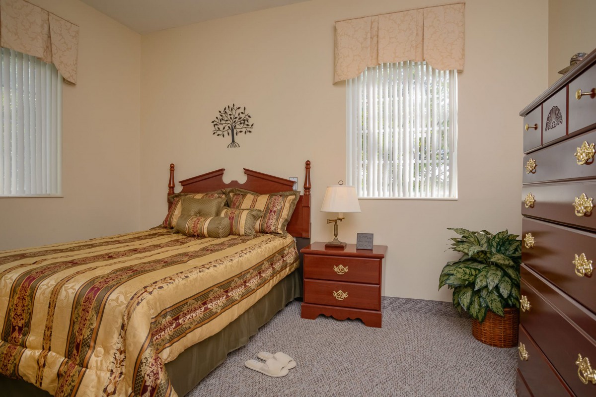 A cozy bedroom with a neatly made bed, nightstand, and lamp next to a window.