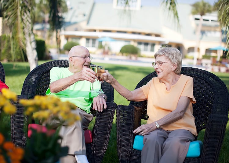An elderly couple enjoying a drink together outdoors in a garden.