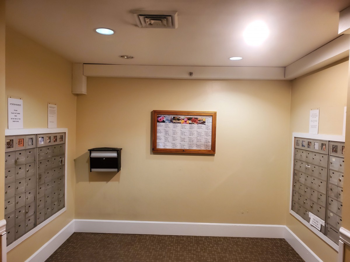 An interior view of a mailroom featuring mailboxes on the walls and a notice board in the center.
