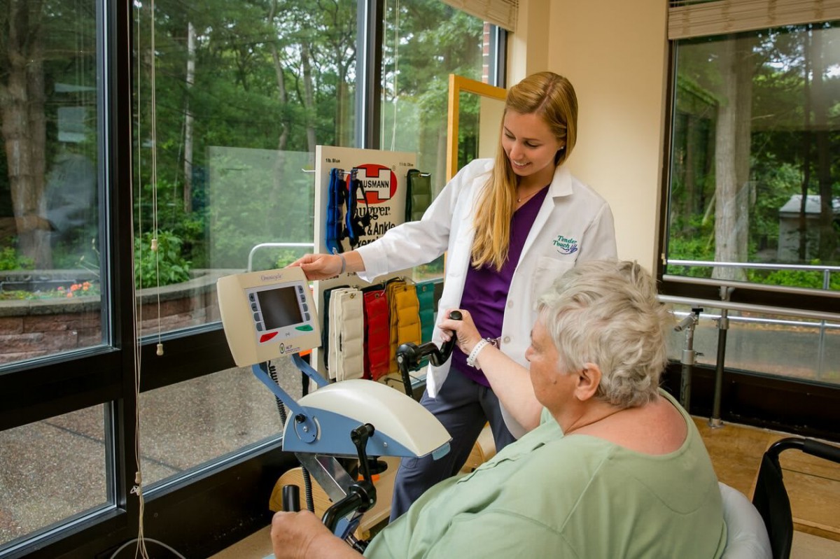 A healthcare professional assists a senior patient with physical therapy exercises using specialized equipment.