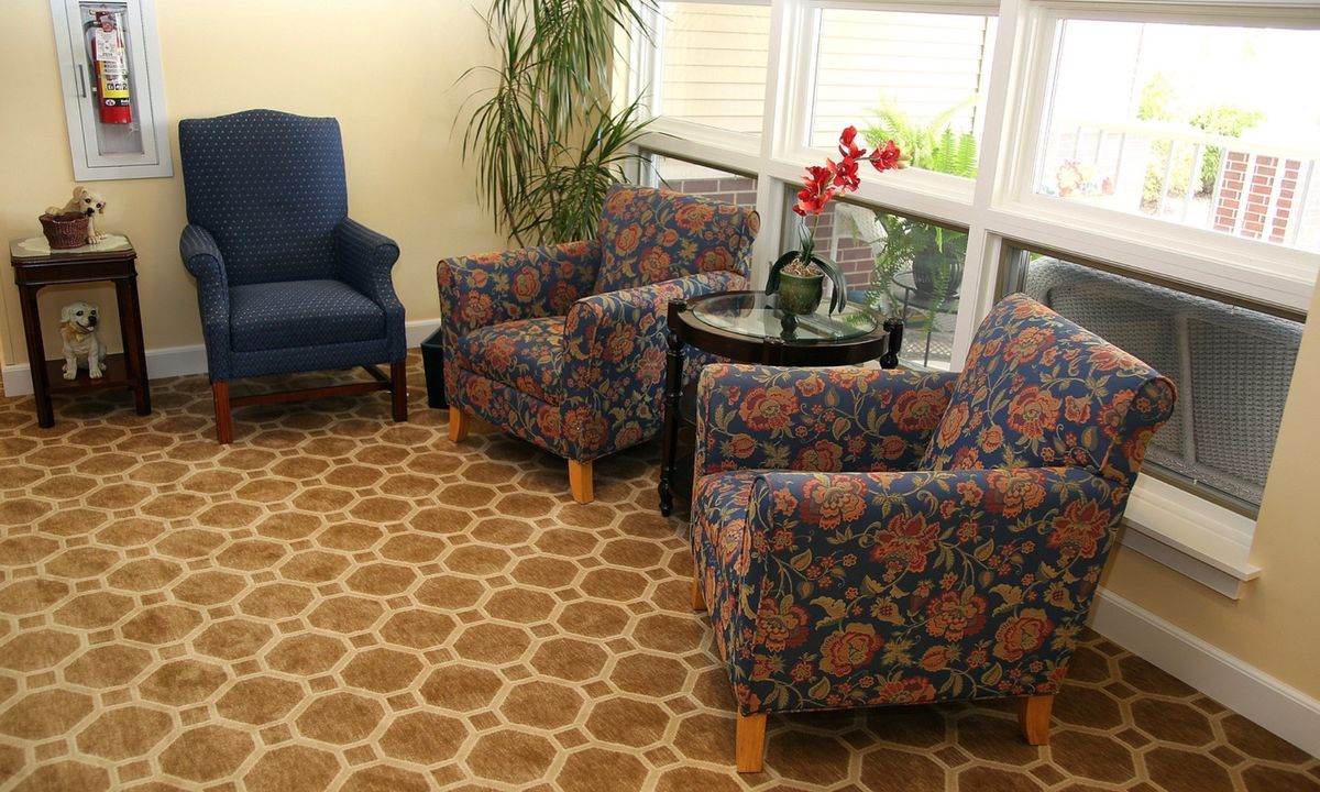 A cozy living room corner with floral patterned chairs, a small table holding an orchid, and a large window providing natural light.