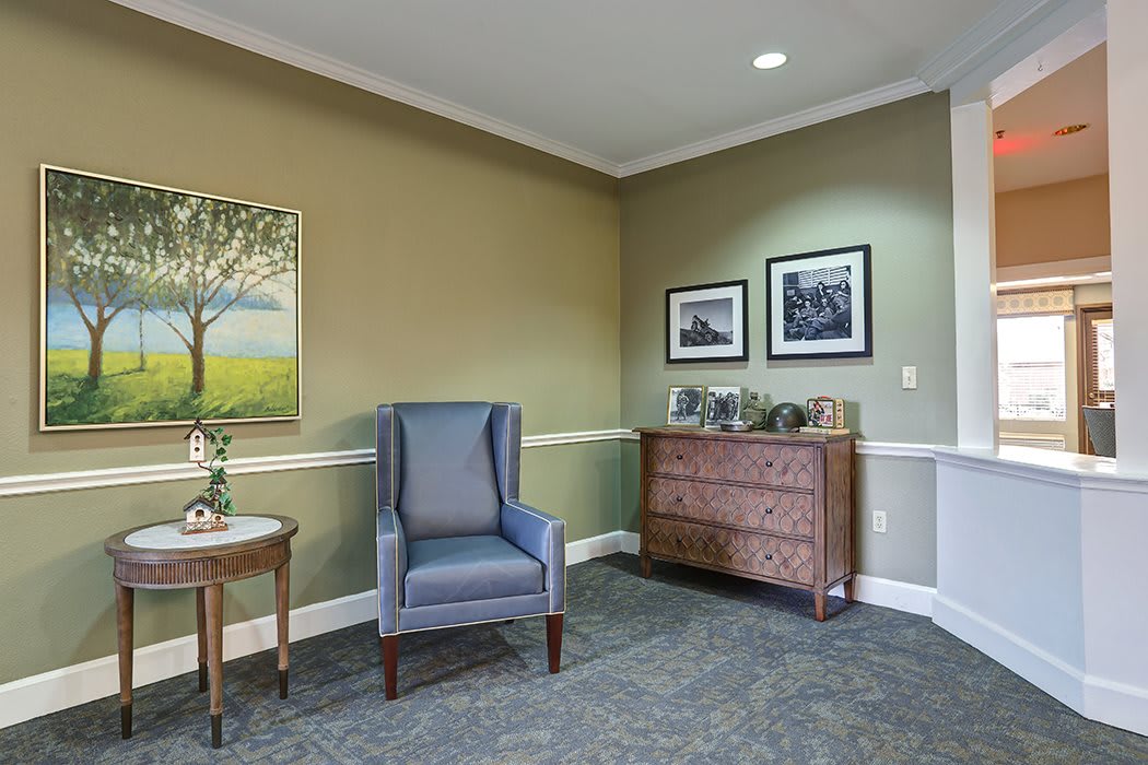 A cozy waiting room corner with a blue armchair, artwork on the walls, and a wooden chest.