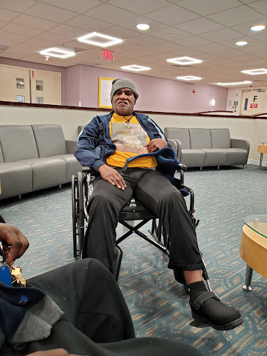 A person seated in a wheelchair in a hospital waiting area.