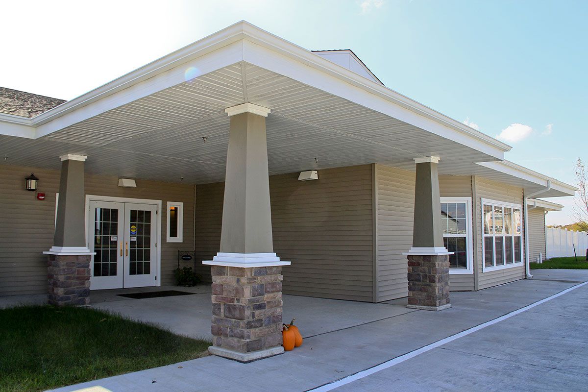 A building entrance with a covered area featuring columns and a pumpkin decoration on the ground.